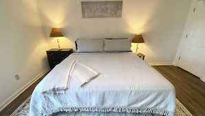 A neatly made bed with a white bedspread and pillows, flanked by two bedside tables with lamps, in a room with a marble floor and a plain wall. - High End Downtown 2-Bed Loft, Pet & Child Friendly (Roanoke)