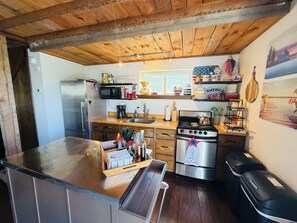 A kitchen with wooden cabinets, a stainless steel refrigerator, a microwave, a stove, and a wooden ceiling.
