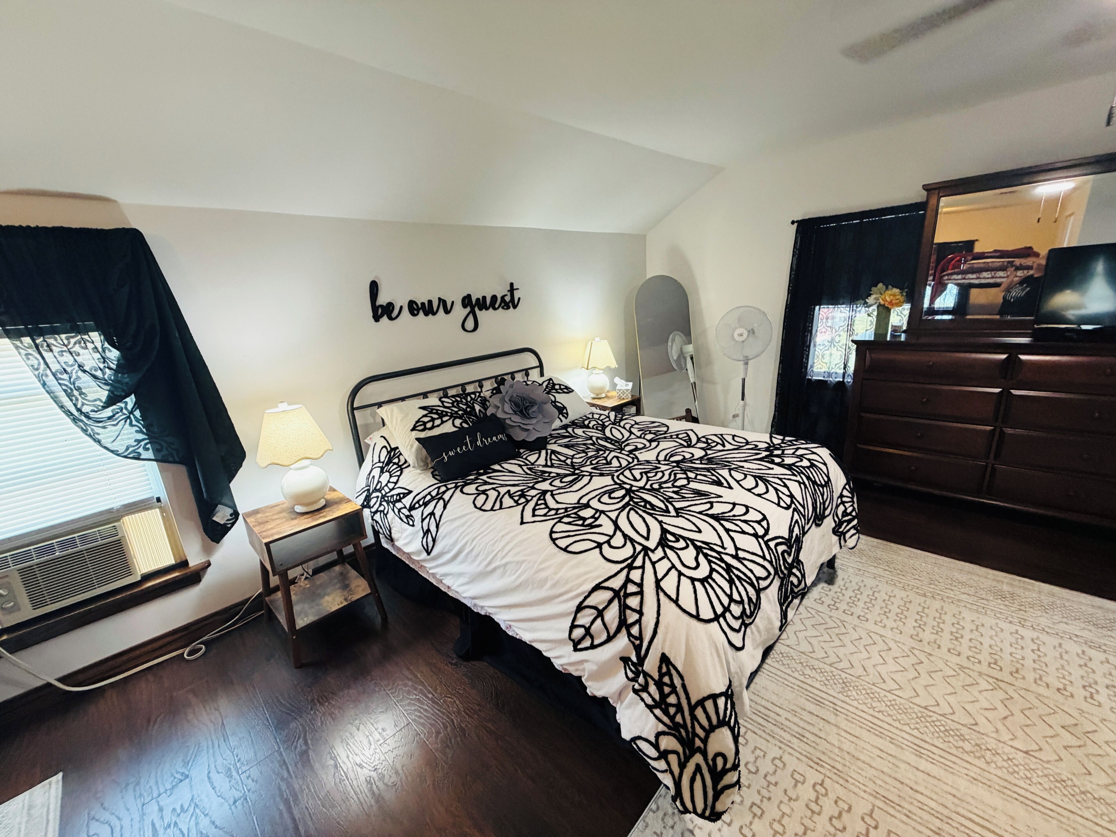 Un dormitorio con cama, lámparas de noche, un reloj de pared, un espejo y un aparador.