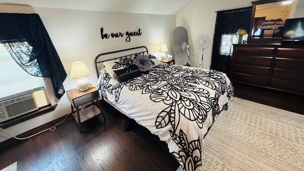 A bedroom with a bed, bedside lamps, a wall clock, a mirror, and a dresser.