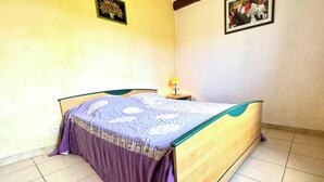 A single bed with a wooden frame and a purple bedspread in a room with plain walls and a tiled floor. - La Devèze - LIMOUX - Gîte (LIMOUX)