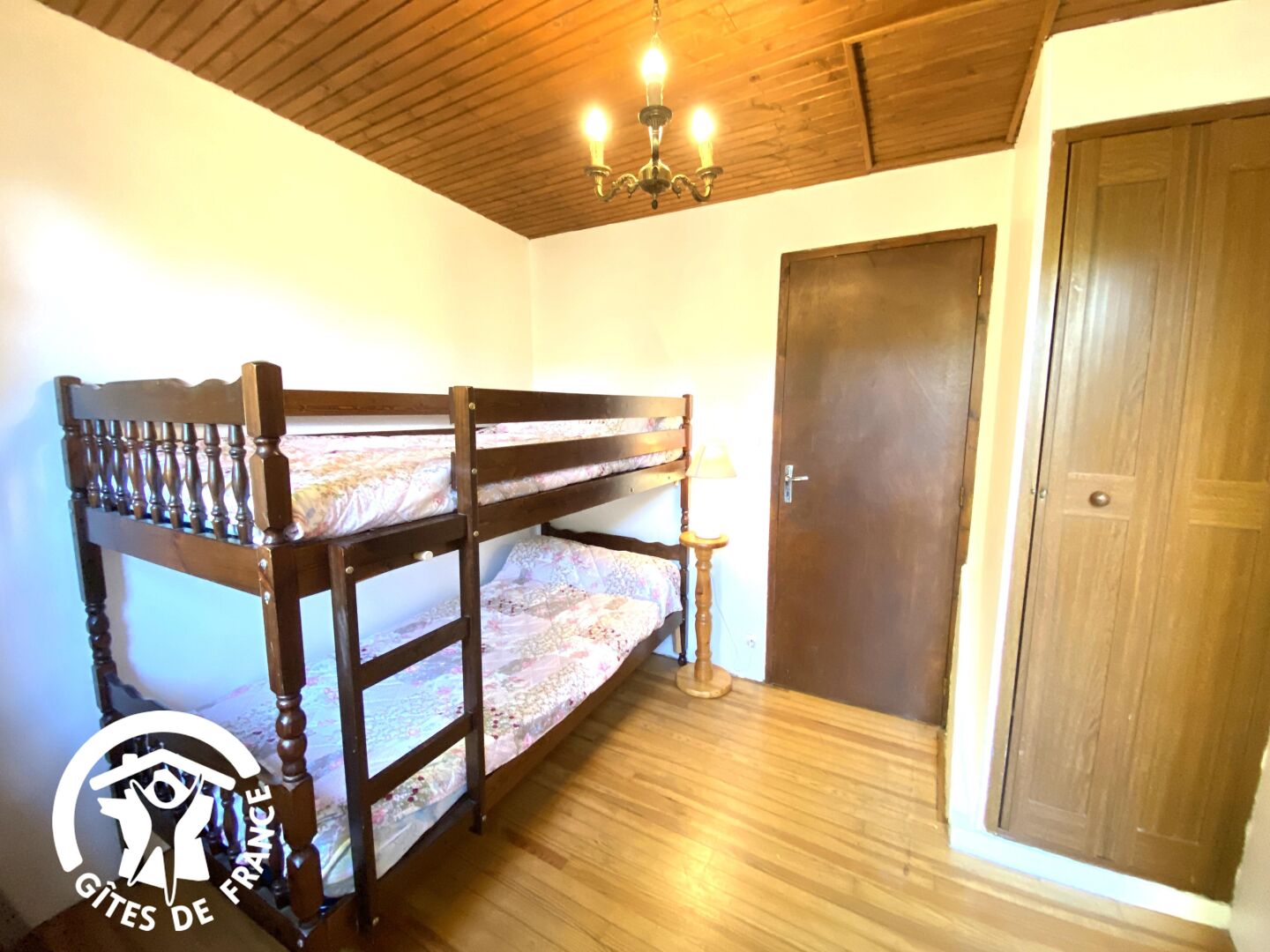 A room with a bunk bed, wooden flooring, a door, and a chandelier.
