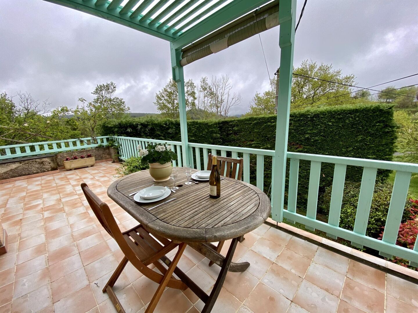 Une terrasse couverte avec une table ronde, des chaises et une bouteille de vin.