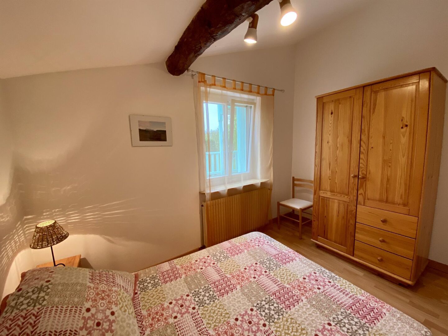 Un dormitorio con una cama, un armario de madera, una silla, una ventana con cortinas y un radiador.