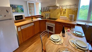 Une cuisine moderne avec des meubles en bois, un four encastré, un four à micro-ondes et un évier. On y trouve une table à manger mise avec des assiettes, des verres et des couverts.