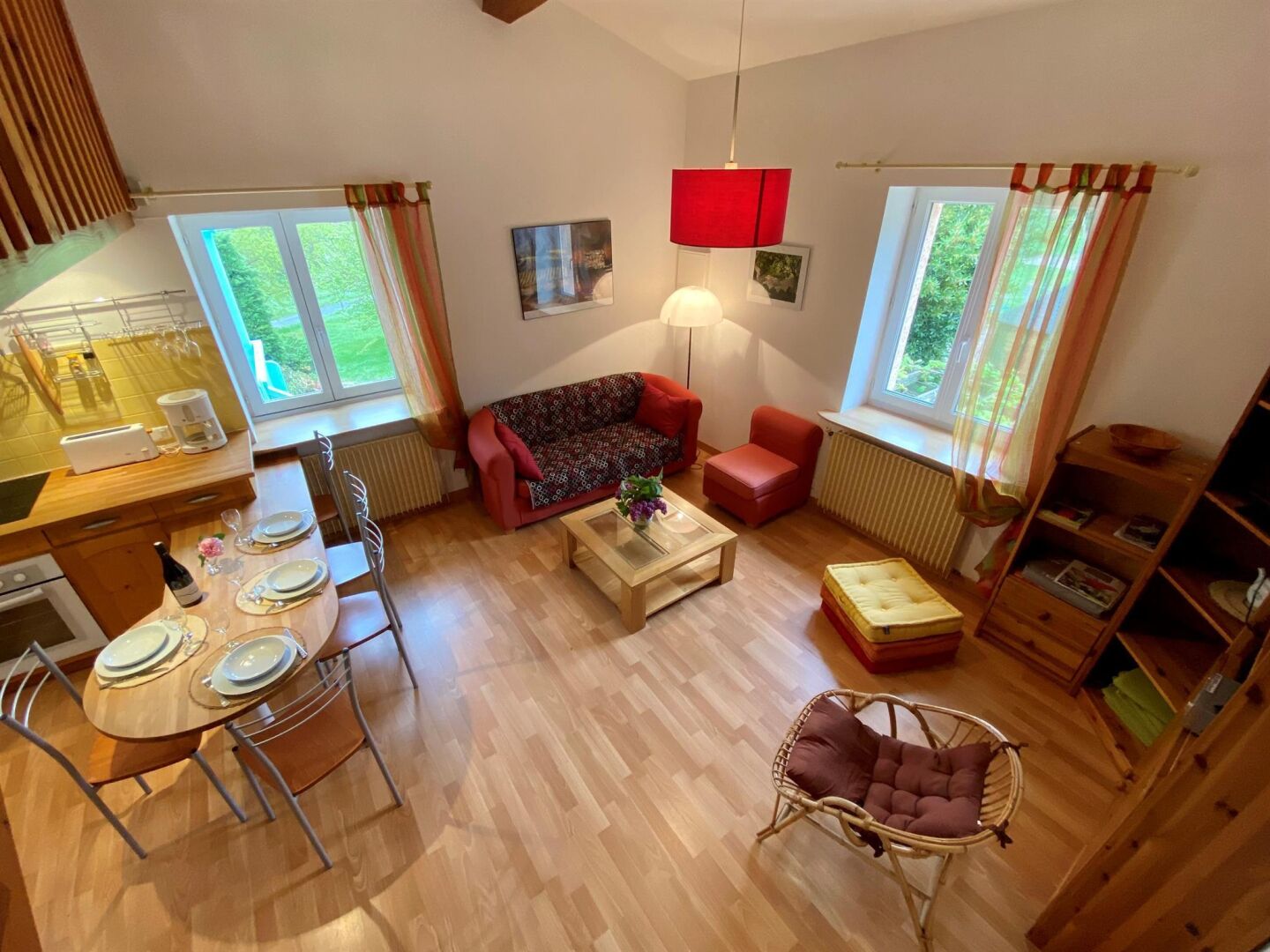 A cozy living room with a sofa, a dining table set for two, and a wicker chair.