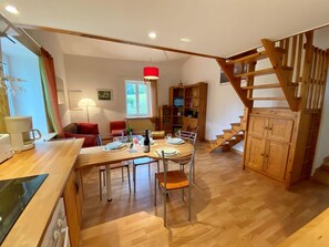 A dining area with a wooden table and chairs, a staircase, and a bookshelf. - Gites les Jendous - RENNES LE CHATEAU (RENNES LE CHATEAU)