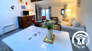 Una sala de estar con un sofá blanco, un aparador de madera, un televisor y un florero con flores sobre una mesa blanca.
