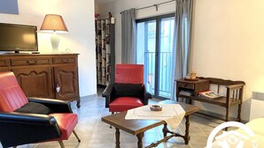 Una sala de estar con televisor, dos sillones, una mesita de centro, una estantería y una ventana con cortinas.