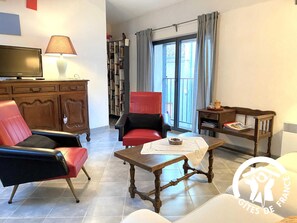 A living room with a TV, two armchairs, a coffee table, a bookshelf, and a window with curtains. - Le Pont Vieux - VILLENEUVE MINERVOIS (VILLENEUVE MINERVOIS)