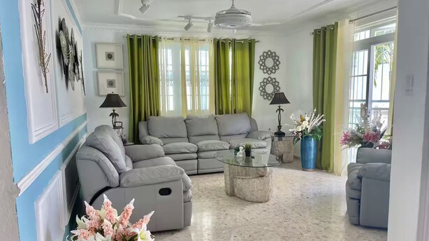 Un salón amplio con un sofá seccional gris, una mesa de centro de vidrio y un jarrón decorativo con flores.