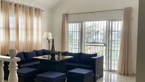 Un amplio salón con un sofá modular grande, una mesa de centro de vidrio y una barandilla blanca.