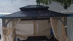 Un espacio de estar al aire libre cubierto, con una mesa y sillas, rodeado por una pérgola con telas colgantes.