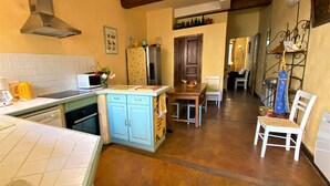 A kitchen with a wooden ceiling, a microwave, a refrigerator, and a dining area with a table and chairs. - Le Faubourg - FERRALS LES CORBIERES (FERRALS LES CORBIERES)