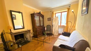 A room with a fireplace, a sofa, a chair, a mirror, and a window with curtains. - Le Faubourg - FERRALS LES CORBIERES (FERRALS LES CORBIERES)