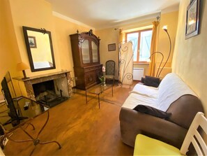 Ein Zimmer mit Kamin, einer Couch, einem Sessel, einem Spiegel und einem fenster mit Vorhängen.