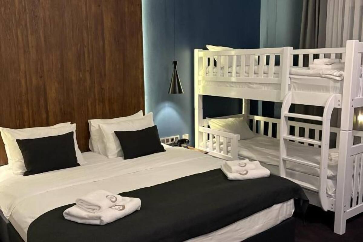A hotel room with a bunk bed, a large bed with white bedding, and a wooden headboard.