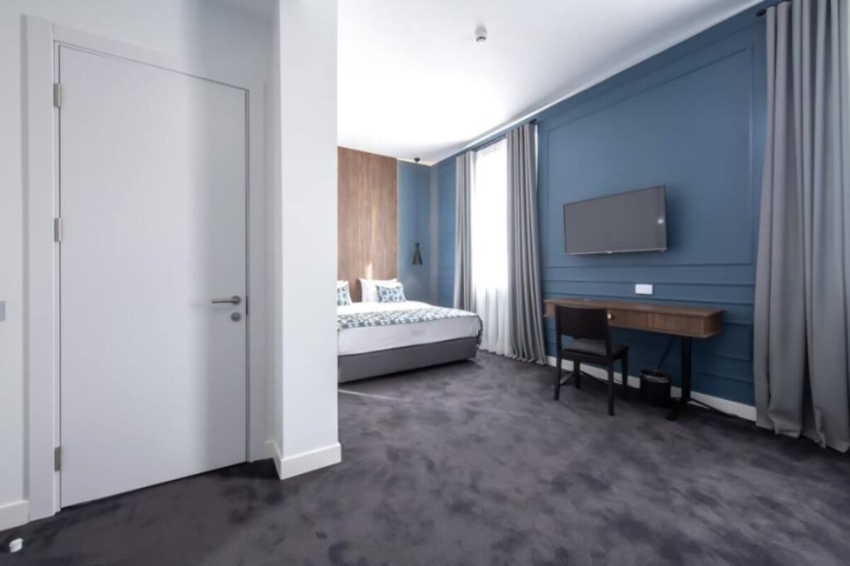 A hotel room with a bed, a desk, and a TV on the wall.