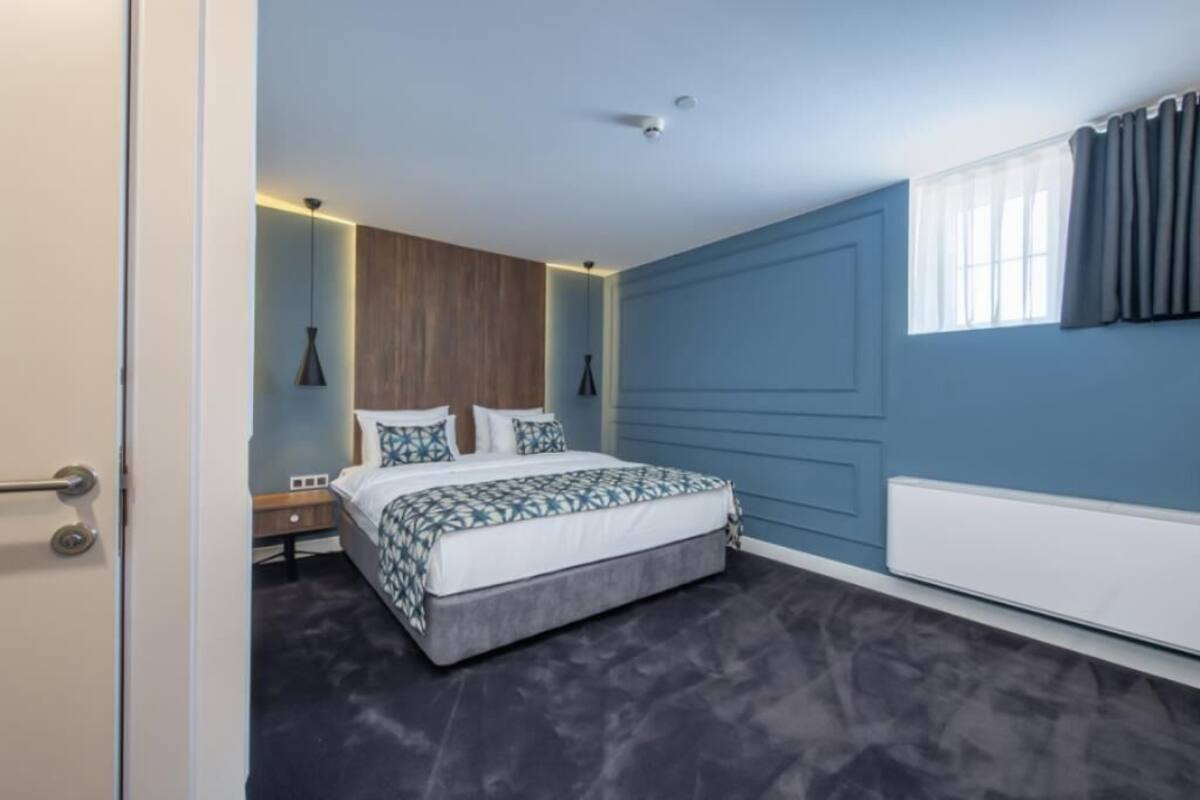 A bedroom with a bed, bedside tables, a window with curtains, and a radiator.