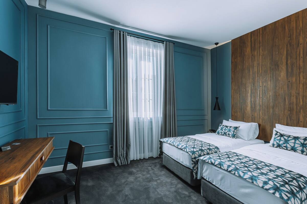 A hotel room with a wooden headboard, two beds with patterned bedding, a desk with a chair, and a television.