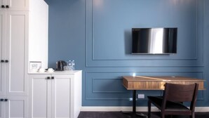 A modern kitchen with white cabinets, a wooden table, and a mounted TV. - Hotel Twenties Tbilisi - Stay & Dine (Tbilisi)