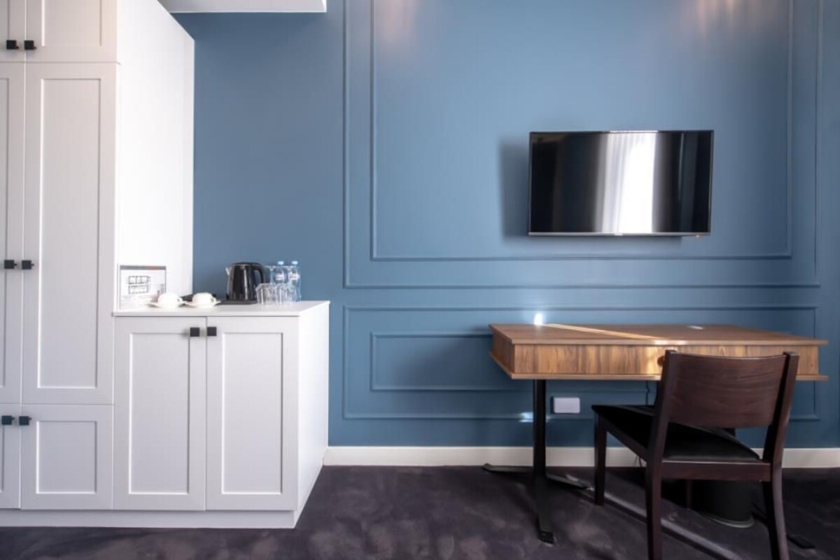A modern kitchen with white cabinets, a wooden table, and a mounted TV.