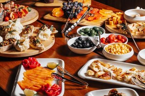 Diversos alimentos en bandejas y recipientes de madera, como queso, frutas y aceitunas.