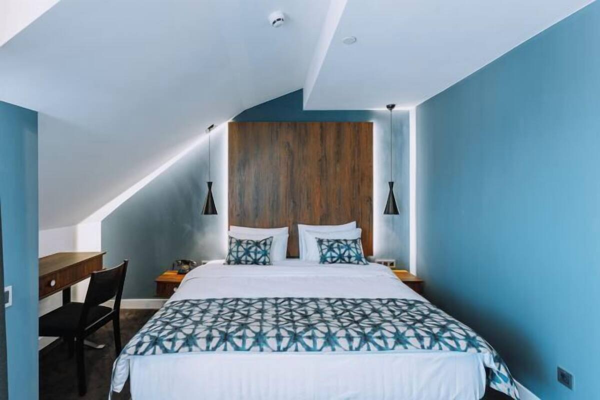 A bedroom with a sloped ceiling, a bed with a geometric patterned bedspread, two bedside lamps, and a wooden headboard.