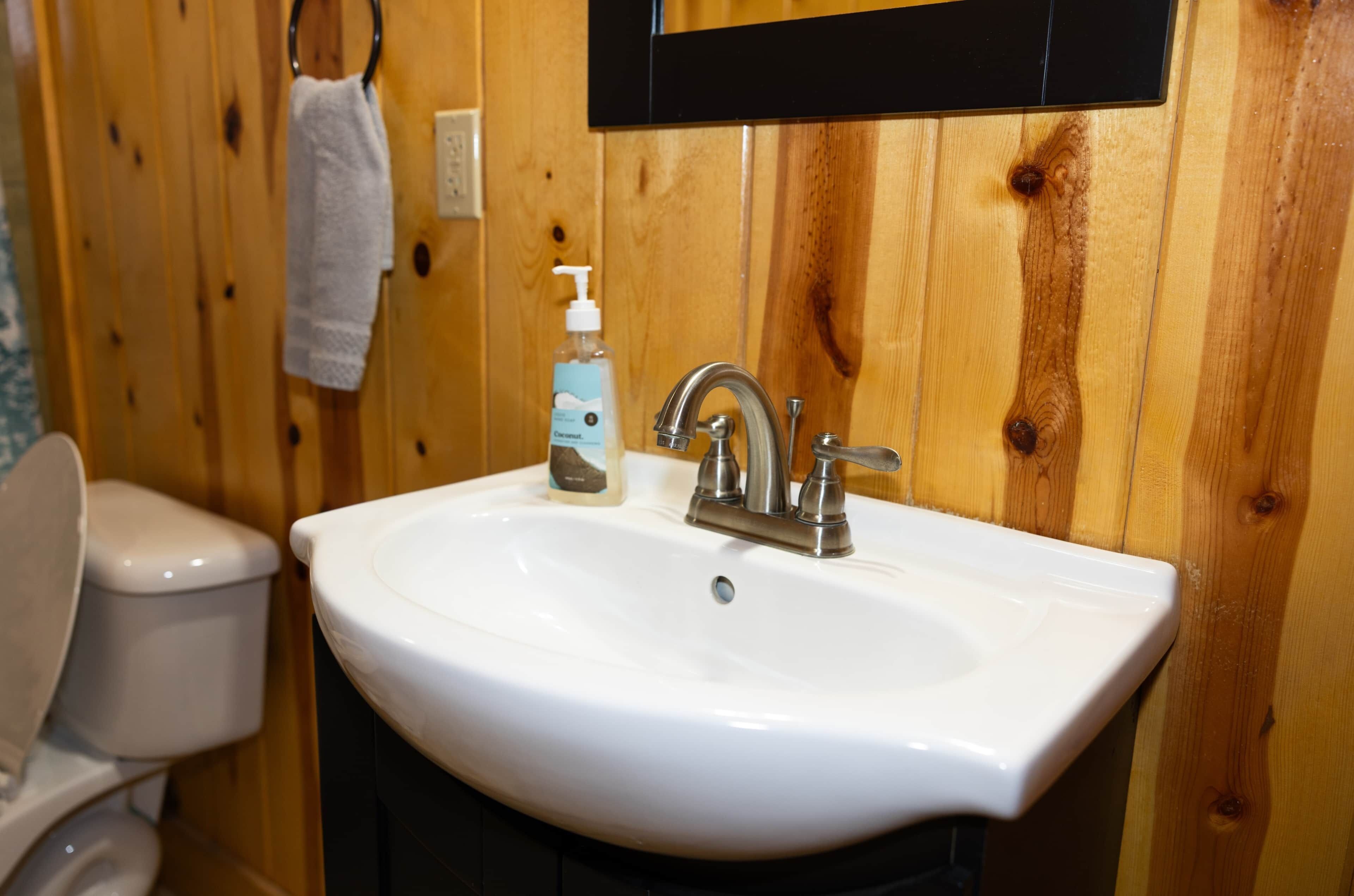 A bathroom with a white sink, wooden walls, a towel hanging on a rack, and a toilet.