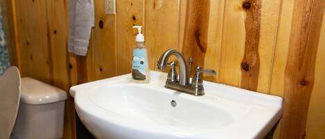 A bathroom with a white sink, wooden walls, a towel hanging on a rack, and a toilet.