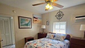 Ein Schlafzimmer mit einem Bett, einem Deckenventilator, einem Fenster mit Jalousien, einer Wandklimaanlage und einer gerahmten Karte an der Wand.