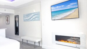 A modern interior with a bench, a fireplace, and two wall-mounted TVs displaying beach and abstract art. - Modern Oceanfront Couple Retreat, SeaWatch 1703 NT (Myrtle Beach)