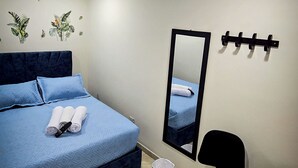 Una camera d'albergo con un letto, una scrivania, una sedia, uno specchio e un gancio a parete.