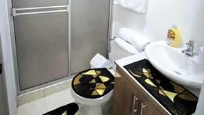 Un bagno compatto con toilette, bidet e lavandino. È presente una zona doccia con porta in vetro e un asciugamano appeso al muro.