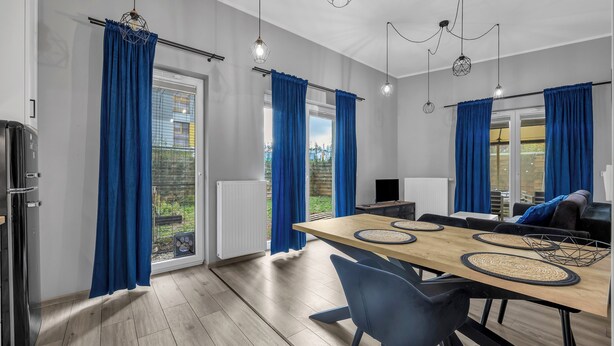 Een moderne keuken met een houten tafel, blauwe gordijnen en hanglampen.