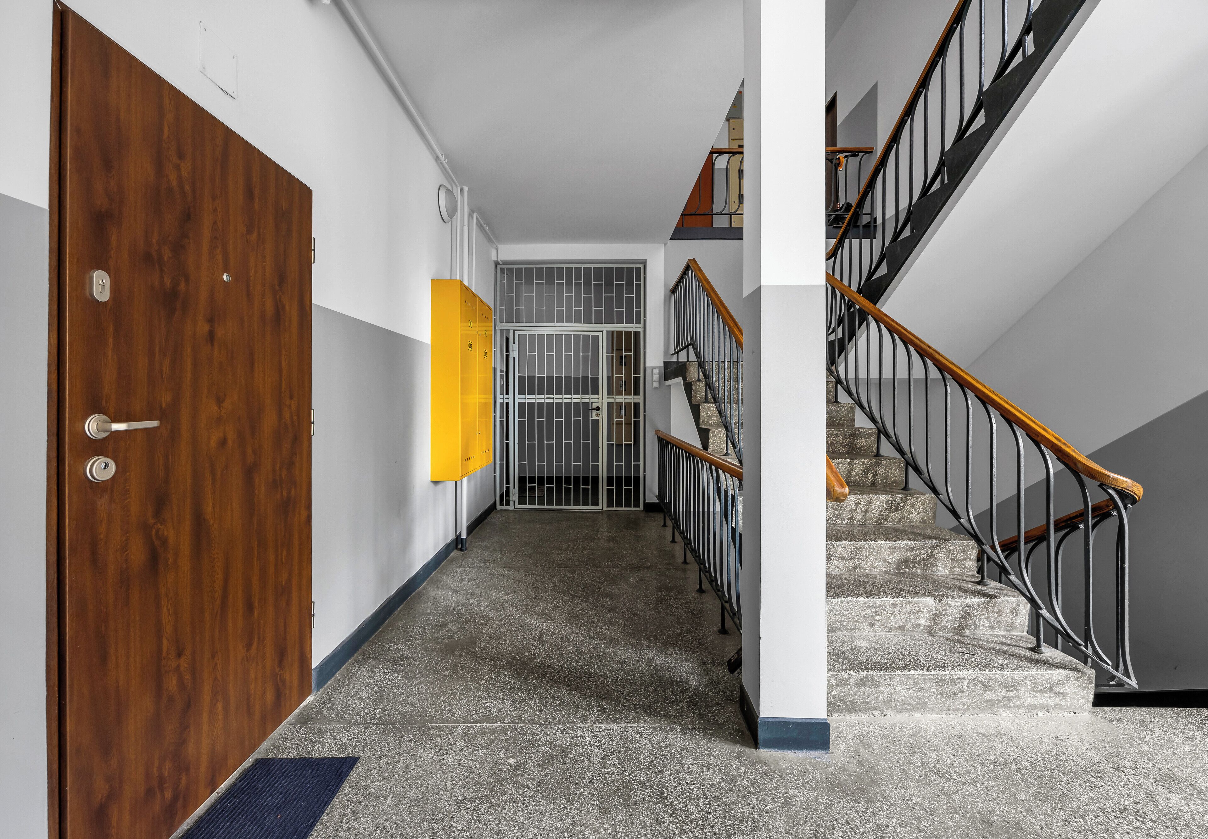 A hallway with a wooden door, a yellow sign, a metal gate, and a staircase with a metal railing.