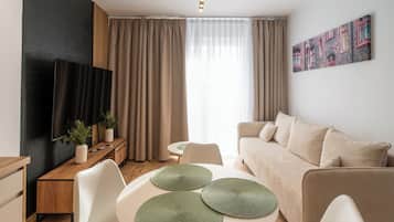 A modern living room with a sofa, a dining table with placemats, a TV on a stand, and a painting on the wall.
