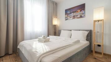 A hotel room with a large bed, a painting of a cityscape, a floor lamp, and a bedside table.