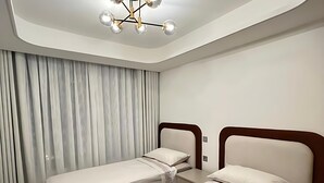 Ein modernes Hotelzimmer mit zwei Einzelbetten, einem großen Fenster mit Vorhängen, einer Deckenleuchte und Holzboden.