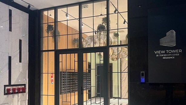 Ein moderner Hotel Eingangsbereich mit Glastür, einer Rezeption und einem digitalen Bildschirm.