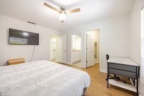 Ein Schlafzimmer mit Bett, Schreibtisch, Deckenventilator und Fernseher.