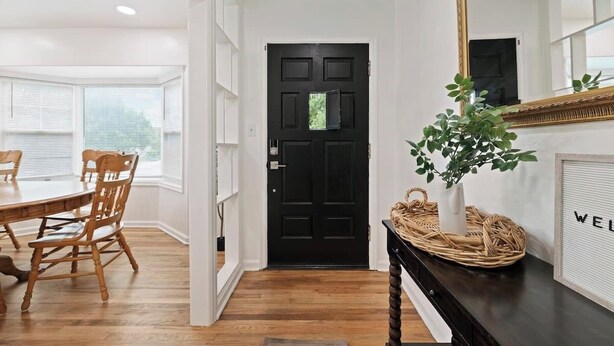 A hallway with a black door, a dining area with wooden chairs and a table, and a mirror on the wall. - Family Retreat Near Trails & Downtown • BBQ, Fire Pit & Kids’ Games (Ogden)