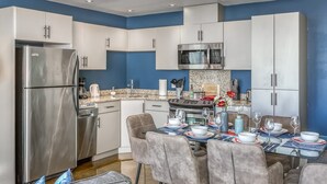 Una cocina moderna con armarios blancos, un refrigerador de acero inoxidable, un microondas y una estufa. Hay una mesa de comedor puesta con platos, vasos y un florero con flores.