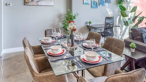 Un comedor con una mesa de vidrio preparada para seis personas, rodeado de sillas de cuero.