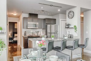 A modern kitchen with stainless steel appliances, a central island with bar seating, and a visible clock on the wall.