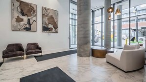 A lobby with two sofas, abstract wall art, a large pillar, and large windows. - Newly Built Modern Condo w Balcony & City Views (Kitchener)