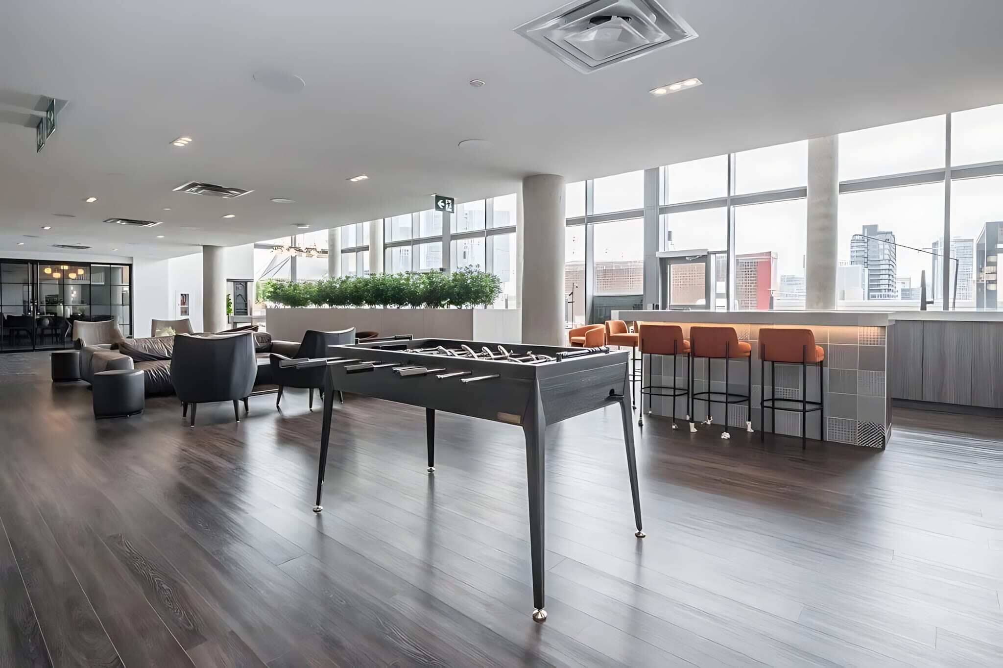 A modern indoor space with a foosball table, seating area, and large windows offering city views.