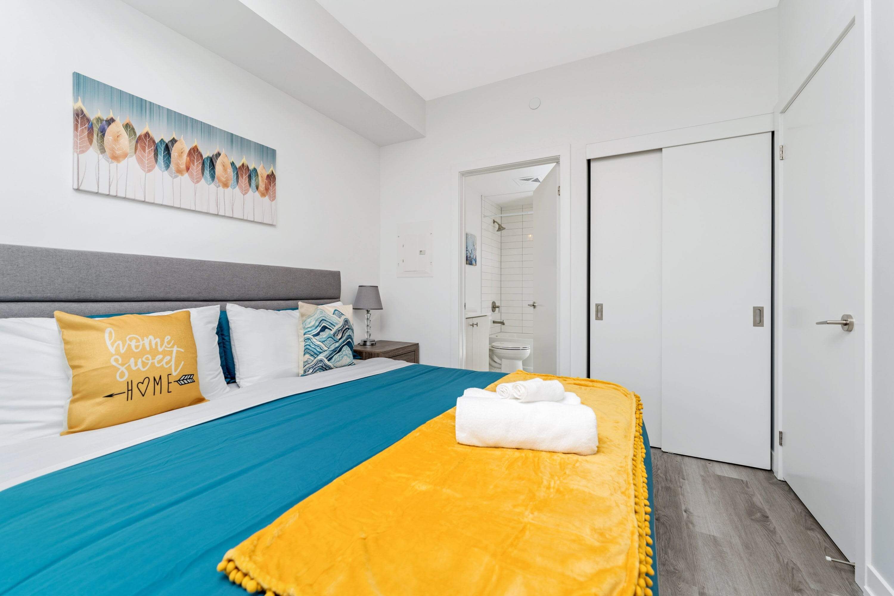 Une chambre d’hôtel avec un lit, un tableau accroché au mur, une porte et une salle de bain visible à travers une porte ouverte.
