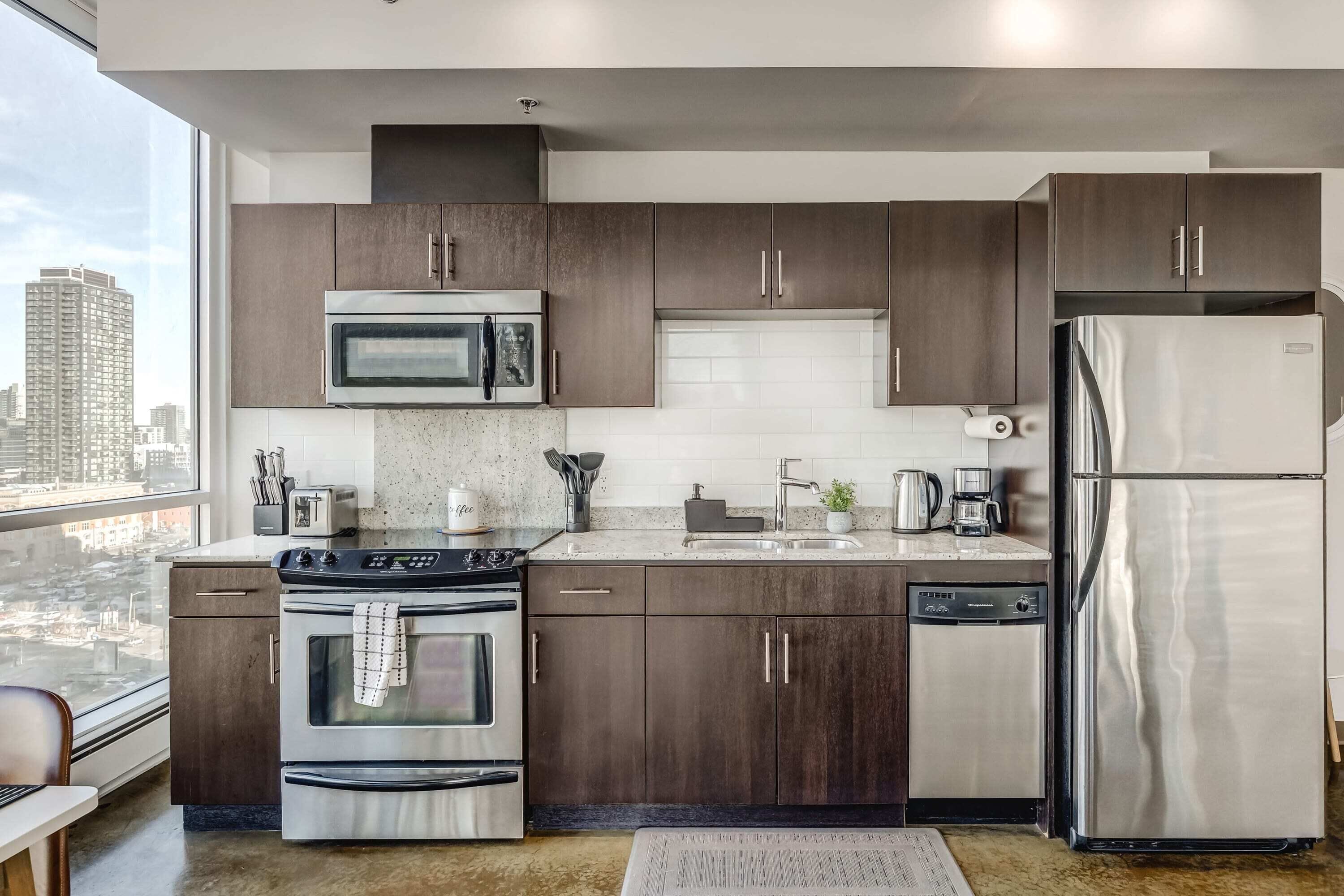 Une cuisine moderne avec des meubles en bois foncé, des appareils électroménagers en acier inoxydable et une grande fenêtre donnant sur la ville.