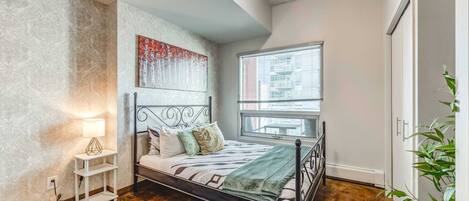 A bedroom with a bed, a nightstand, a window, and a plant.